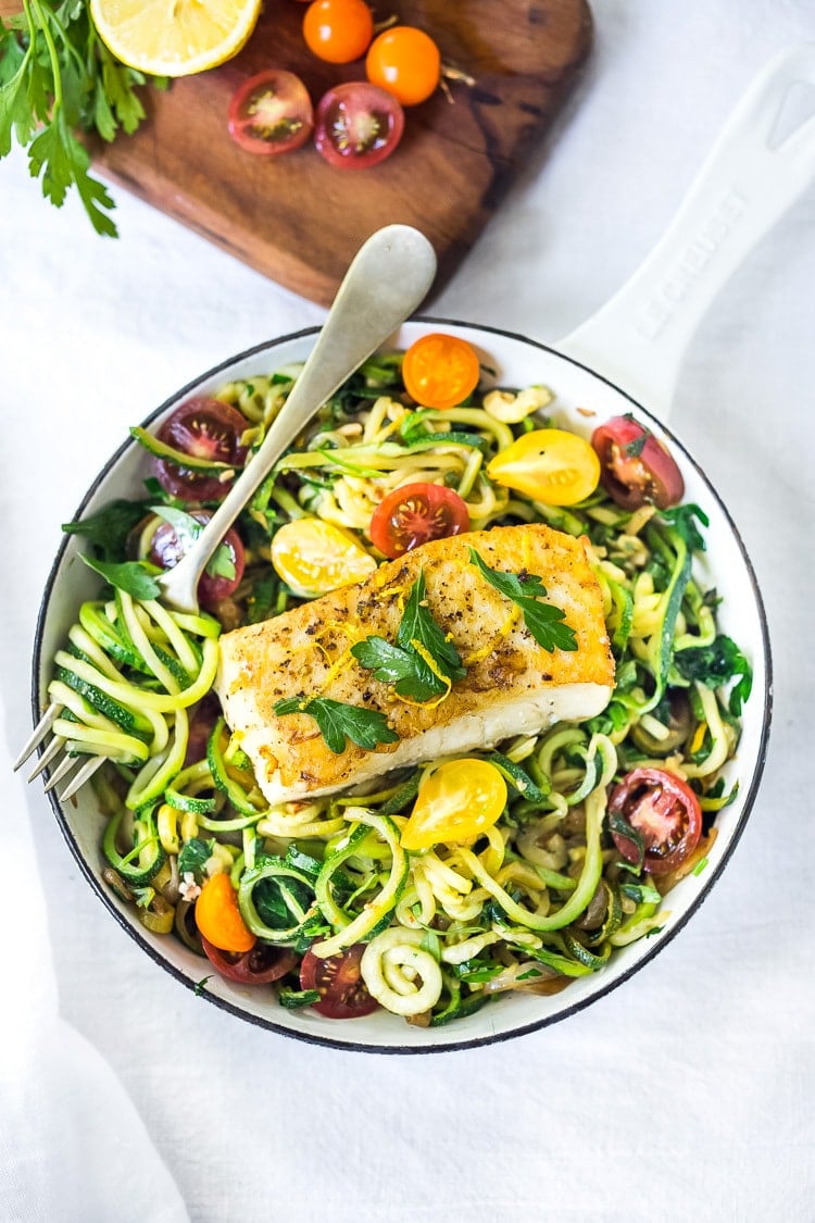 single serving pan with zucchini noodles and summer sweet tomatoes topped with halibut, garnished with parsley and lemon zest. 